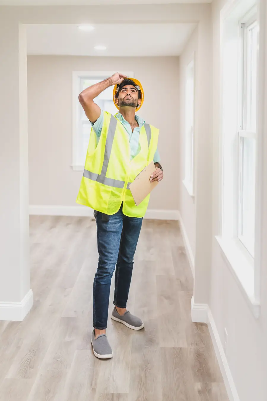 Man in a hard hat and safety vest checking a ceiling inside a house