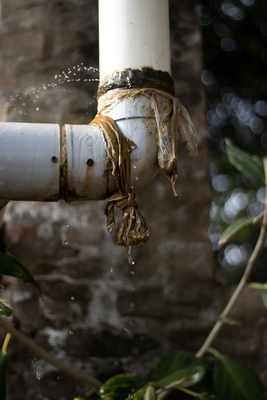 Pipe joint wrapped in plastic with water dripping from the leak